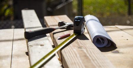 House plans, hammer and measuring tape sitting on wooden deck surface under construction