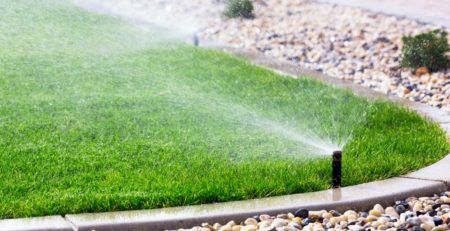 Lawn sprinkler watering green lawn with rock landscaping around it