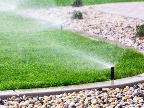 Lawn sprinkler watering green lawn with rock landscaping around it